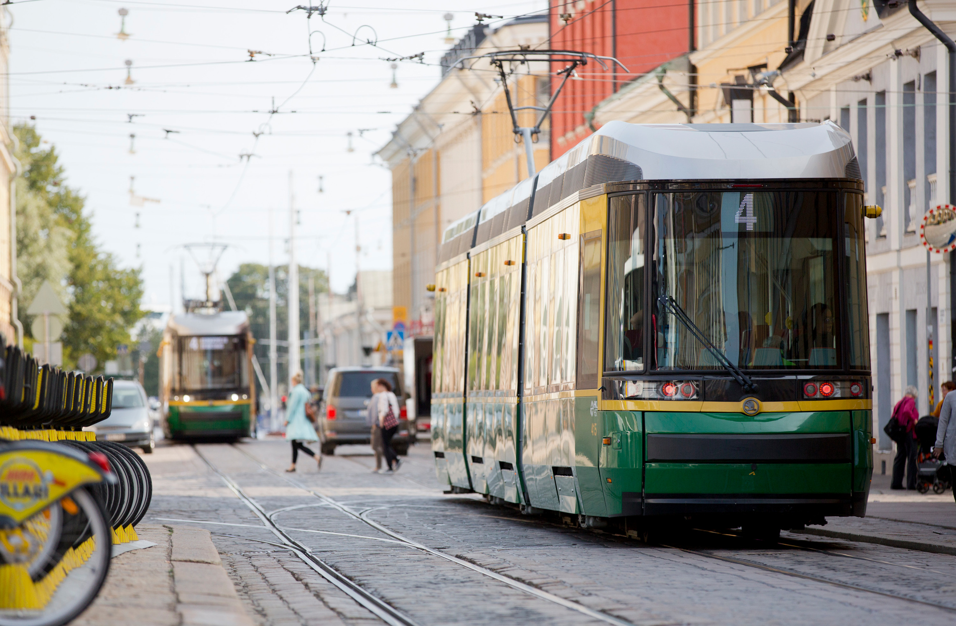 Raitiovaunu ajaa katua pitkin. Jalankulkijat ylittävät kadun